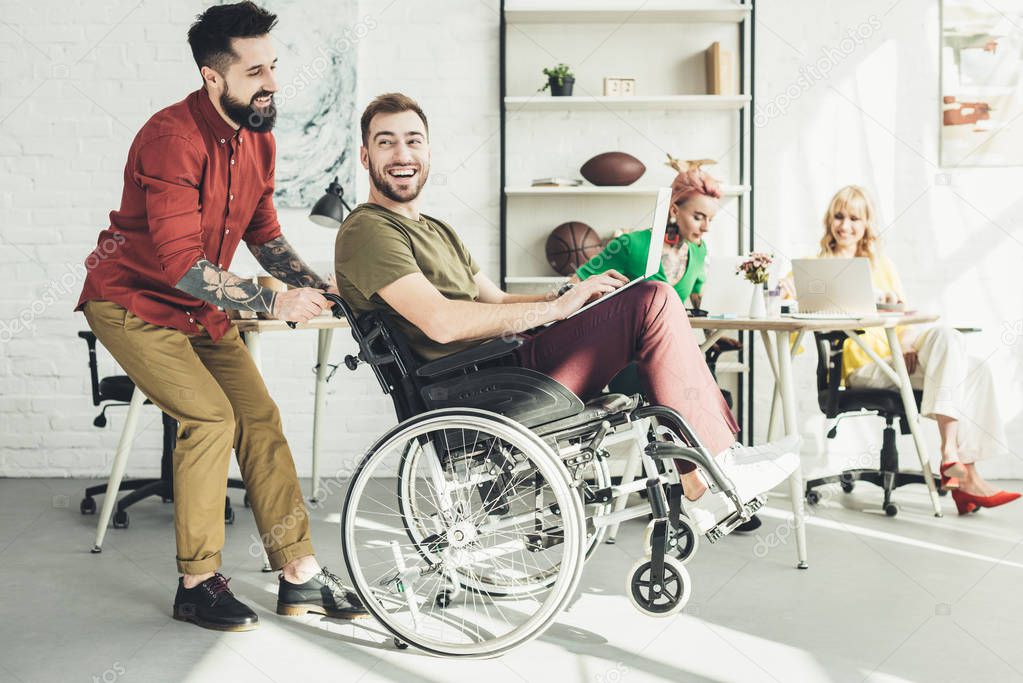 disabled businessman with laptop with colleague near by and businesswomen behind in office 