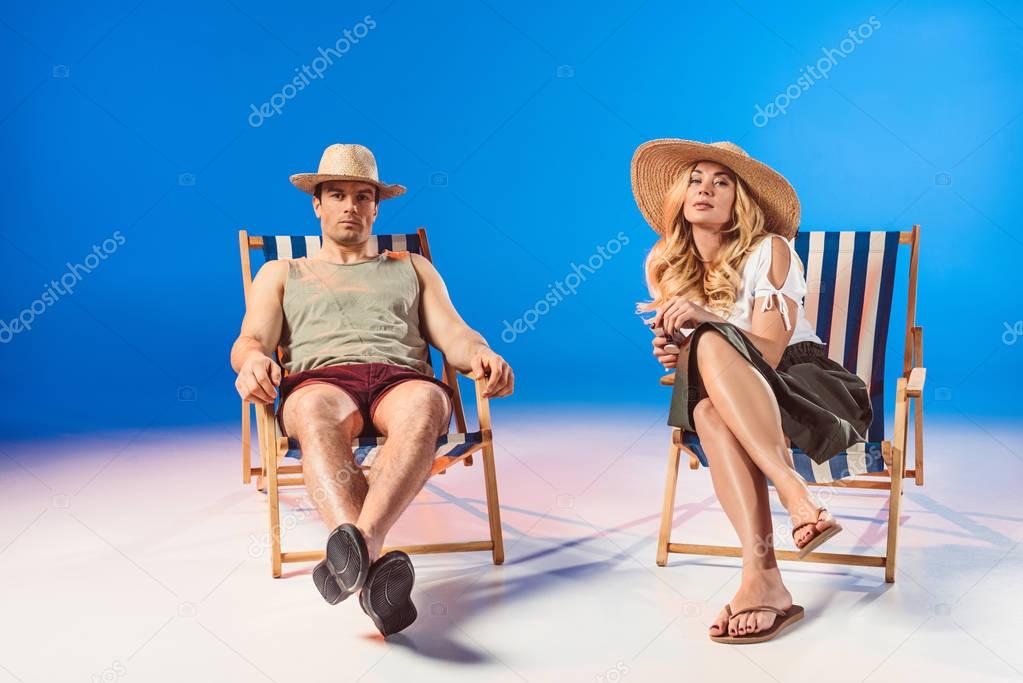 Young couple resting in deck chairs on blue background