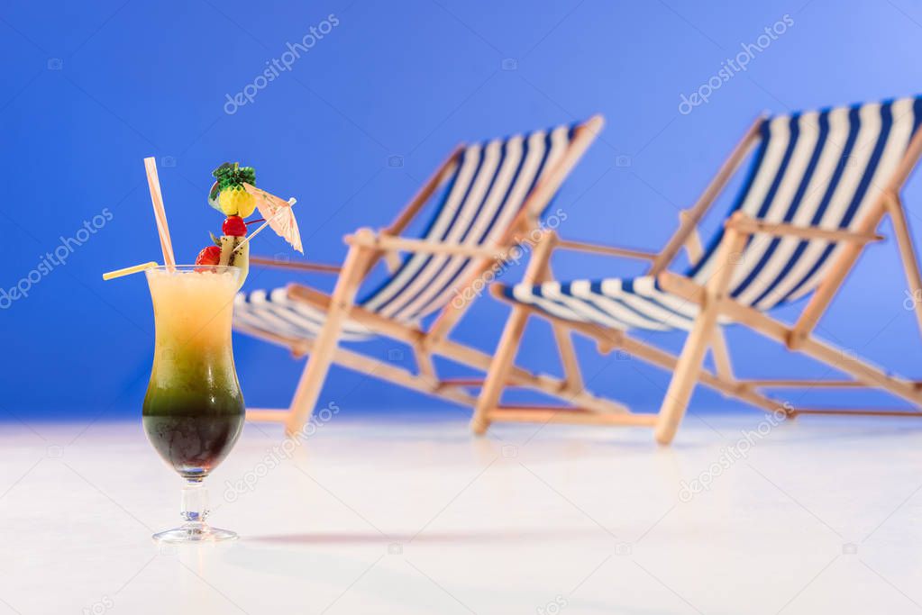 Cocktail in glass by deck chairs on blue background