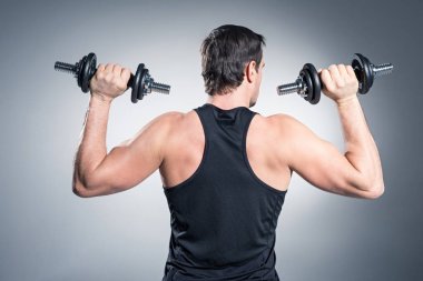 Arkadan görünüş adamın gri arka plan üzerinde dumbbells ile egzersiz