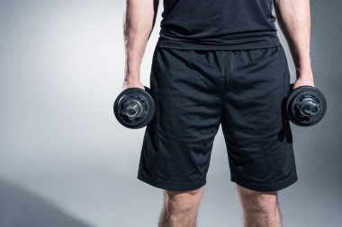 Adam gri arka plan üzerinde dumbbells ile eğitim görmek