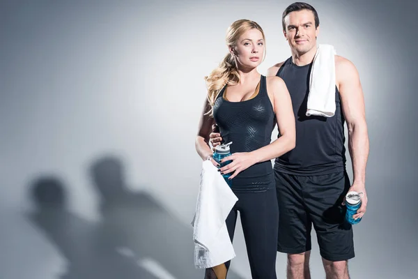 Sportliches Paar Mit Handtüchern Und Wasserflaschen Vor Grauem Hintergrund — Stockfoto