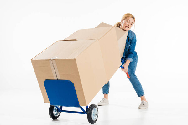 Attractive woman trying to push delivery cart with boxes isolated on white