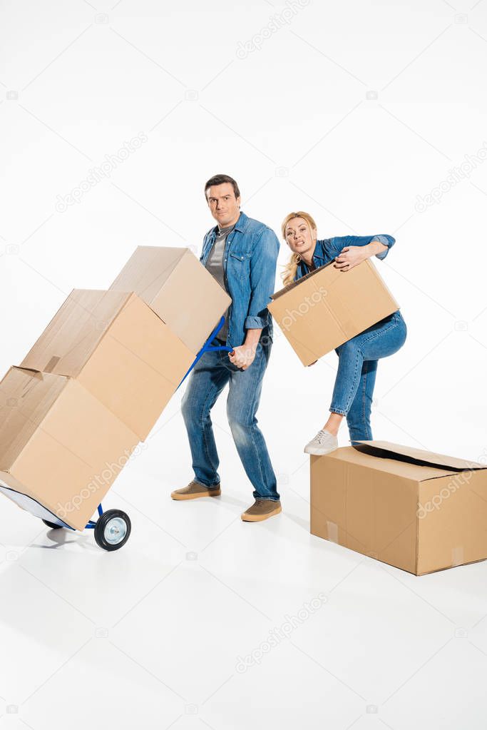 Young couple moving cardboard boxes with trolley cart isolated on white