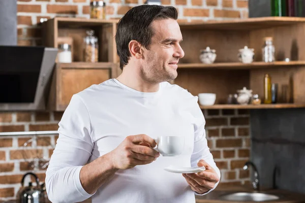 Homem Bonito Sorrindo Olhando Para Longe Enquanto Bebe Café Cozinha — Fotografia de Stock Grátis