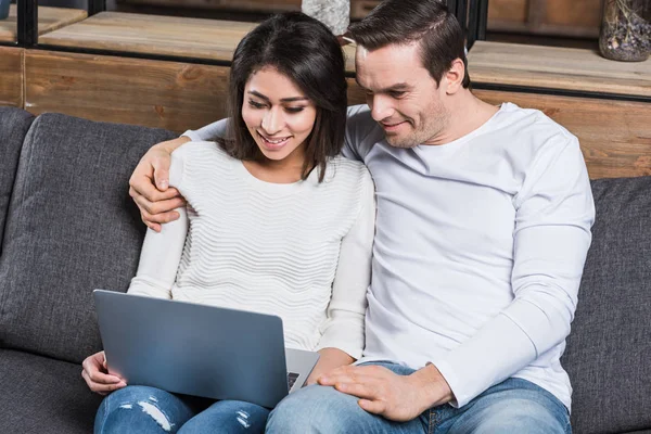 Sorrindo Casal Multiétnico Usando Laptop Juntos Enquanto Sentado Sofá Casa — Fotos gratuitas