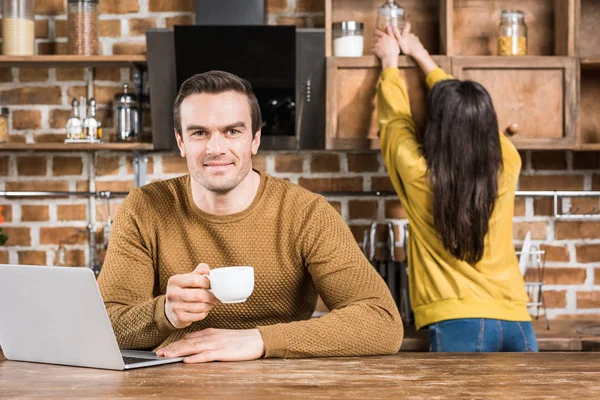 Handsome Young Man Holding Cup Coffee Smiling Camera While Using — Free Stock Photo