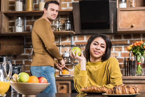 Elma Tutarak Kamera Arkasında Kahvaltı Hazırlarken Kocası Ise Gülümseyen Güzel — Ücretsiz Stok Fotoğraf