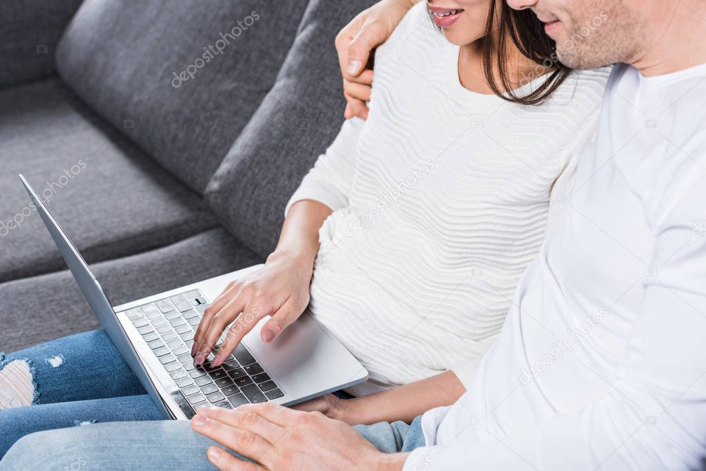 cropped shot of multiethnic couple using laptop while sitting together on couch