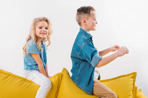 boy pretending to be a driver while sitting on sofa with sister