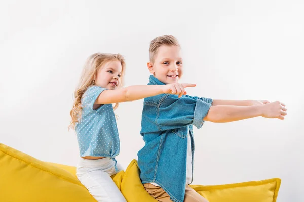 Little Boy Driving Sister Pointing While Sitting Yellow Sofa — Free Stock Photo