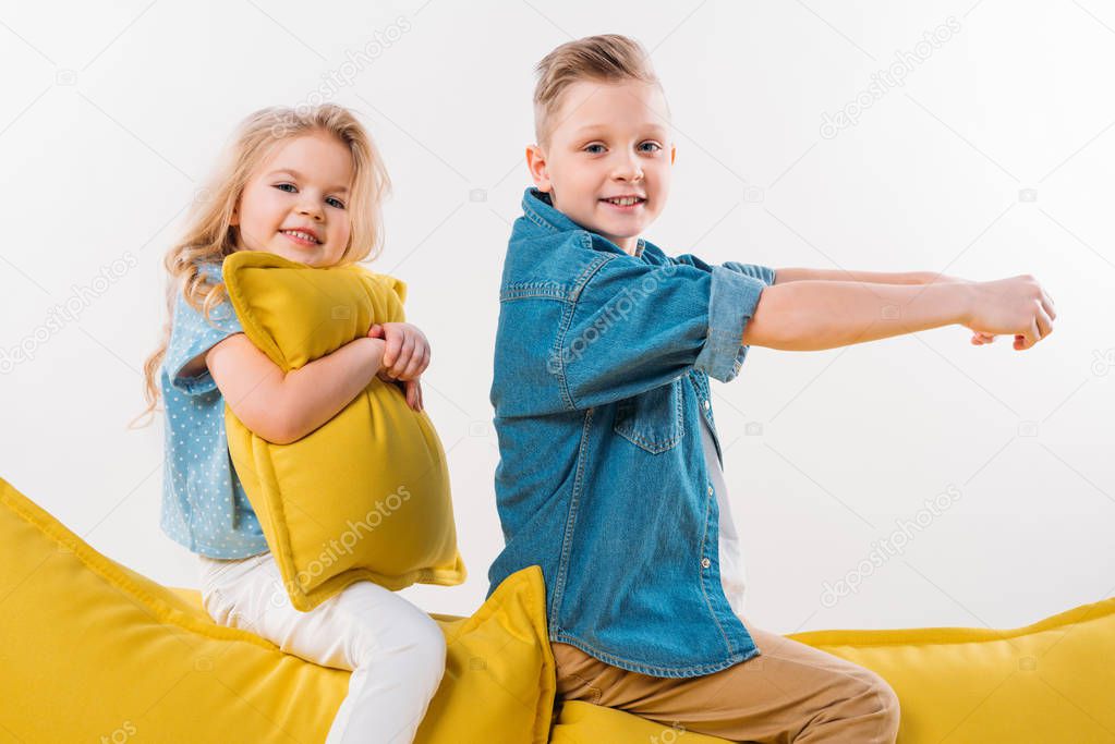 happy boy pretending to be a driver while sitting on yellow sofa with sister