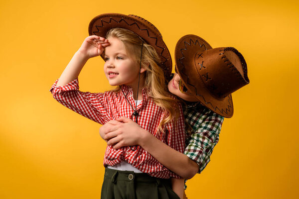 little cowboy embracing stylish cowgirl, isolated on yellow