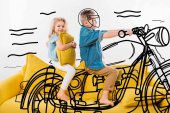 Boy předstírá biker a motocykl na koni v sedle na žluté pohovce se sestrou