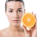 Attractive naked girl with clean skin holding half of orange isolated on white