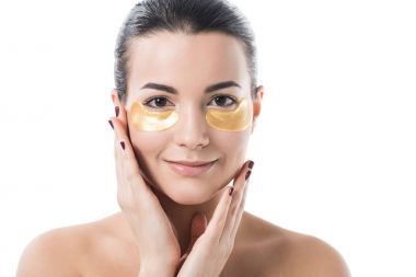 gözleri yamalar üzerinde beyaz izole kamera bakarak altında nemlendirici ile gülümseyen güzel kız