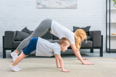Side view of mother and son in adho mukha svanasana position on yoga mats clipart