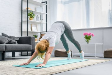 Woman in downward facing dog position on yoga mat clipart