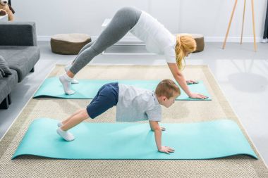 Side view of mother and little son in adho mukha svanasana position on yoga mats clipart