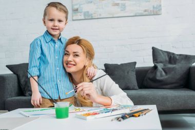Küçük çocuk kucaklayan anne o boya fırçası tutan süre 