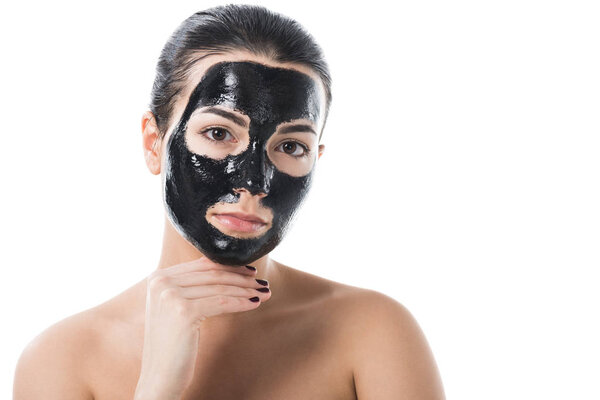 attractive girl in cosmetic black clay facial mask looking at camera isolated on white