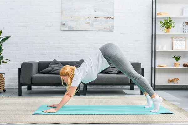 Side view of young woman in adho mukha svanasana position on yoga mat