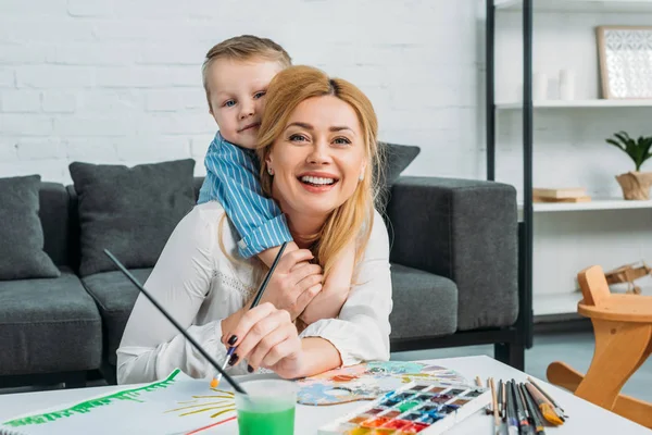 Pequeño Hijo Abrazando Sonriente Madre Mientras Ella Pintando Casa — Foto de Stock