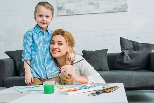 Little Boy Embracing Mother While She Holding Paintbrush — Stock Photo, Image