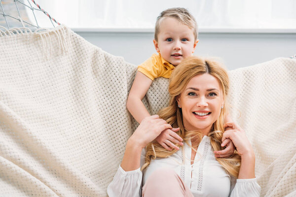 Little boy embracing smiling mother while she laying in hammock 