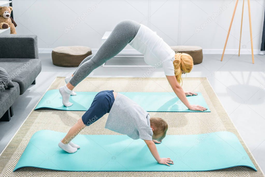 Mother and little boy practicing downward facing dog position on yoga mats