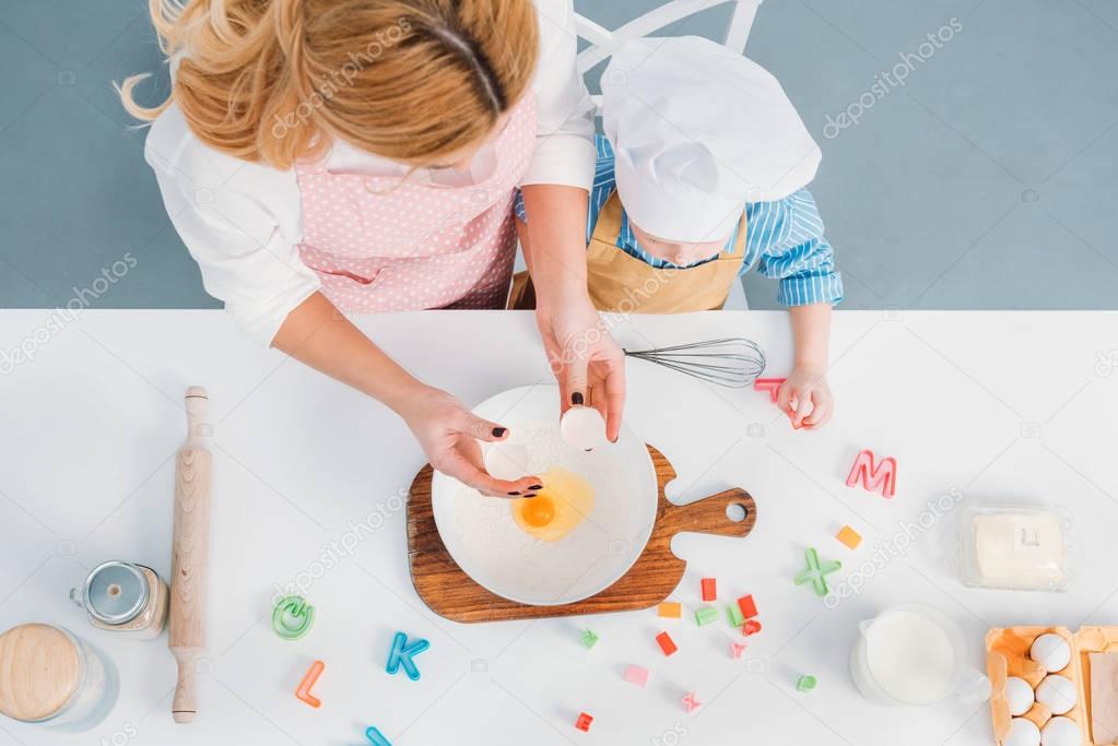 Top view of mother and son pouring egg into bowl with flour 