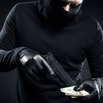 Человек в черной балаклаве держит пистолет и доллары