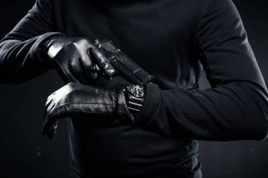 Man in gloves with gun checking his watch  clipart