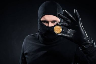 Man in black balaclava holding golden bitcoin clipart