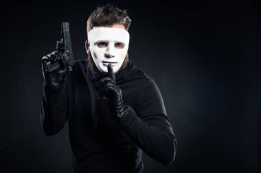 Thief in mask holding gun and showing silence gesture clipart