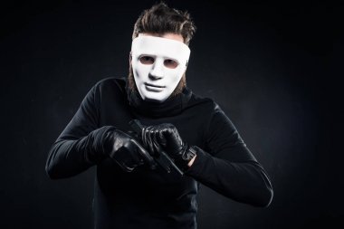 Robber in white mask and black clothes recharging his gun clipart