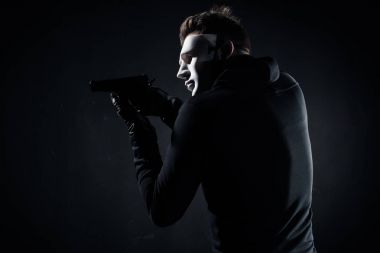 Robber in mask and gloves aiming with gun on black clipart