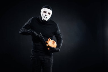 Burglar in mask holding gun and piggy bank clipart