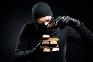 Robber in balaclava stacking gold bullions in his hands clipart