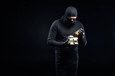 Thief in balaclava stacking gold ingots in his hands clipart