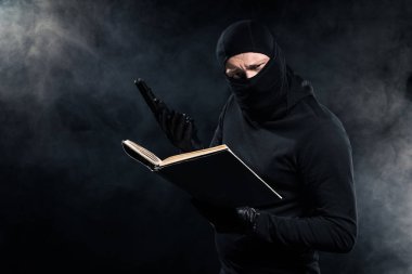 Adam siyah yün holding silah ve kitap okumak