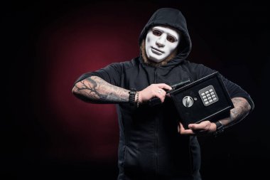 Burglar in mask holding gun and locked safe clipart