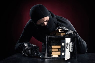 Man in balaclava with gun stealing gold bullions from safe clipart