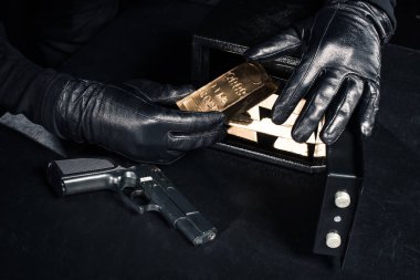 Close-up view of robber with gun taking gold bars from safe clipart
