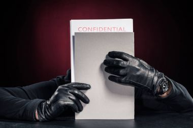 Criminal in black gloves holding confidential documents clipart
