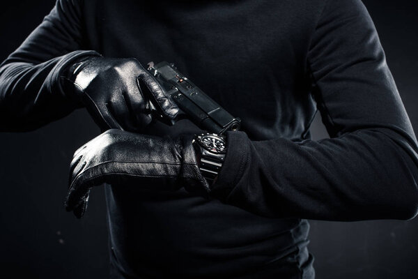 Man in gloves with gun checking his watch 