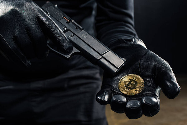 Close-up view of gun and bitcoin in hands of thief