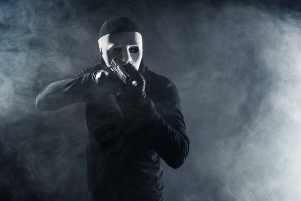 Man in mask and balaclava aiming with gun and flashlight
