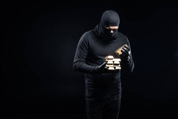 Thief in balaclava stacking gold ingots in his hands