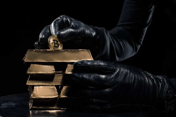 Close-up view of golden bars and bitcoin in hands of thief